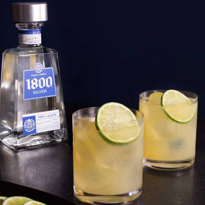 bottle of 1800 silver tequila reserva 2 glasses poured with lime and ice