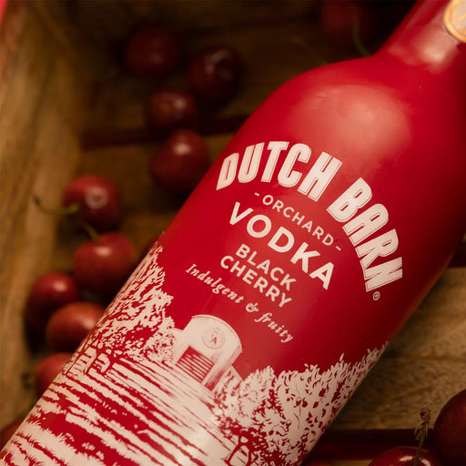 Red bottle of Dutch Barn Vodka Black Cherry with cherries in the background