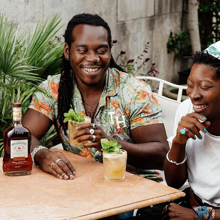 Two people sitting at a table with cocktails and a bottle of Appleton Estate rum.