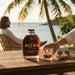 Bottle of Papa's Pilar Dark Rum on a table by a waterfront with palm trees