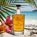 Bottle of Birthday Queen spiced rum on a beach with flowers and palm leaves.
