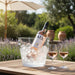 Bottle of AIX rosé wine in a bucket of ice with two glasses on a wooden table outdoors.