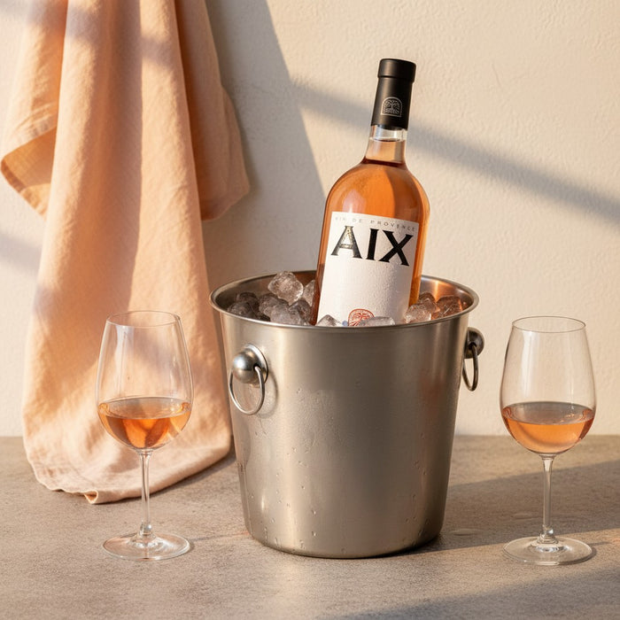 Bottle of AIX wine in an ice bucket with two glasses on a table.