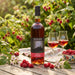 Bottle of Afon Mél mead with two glasses on a table outdoors surrounded by raspberries.