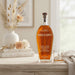 Bottle of Angels Envy whiskey on a wooden surface with a glass and decorative items in the background.