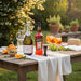 Outdoor setting with a wooden table set for a meal, featuring bottles of wine and Aperol, glasses of orange juice, and oranges.