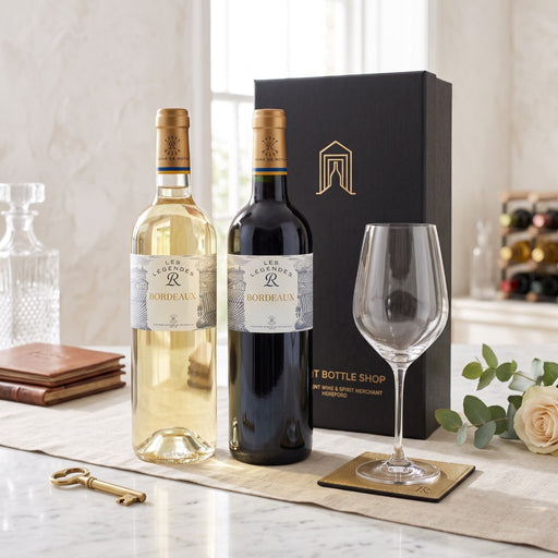 A wine gift set featuring a bottle of Les Legendes Bordeaux white wine, a bottle of Les Legendes Bordeaux red wine, a black gift box with gold lettering, and a clear wine glass on a marble table with decorative props.