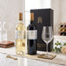 A wine gift set featuring a bottle of Les Legendes Bordeaux white wine, a bottle of Les Legendes Bordeaux red wine, a black gift box with gold lettering, and a clear wine glass on a marble table with decorative props.