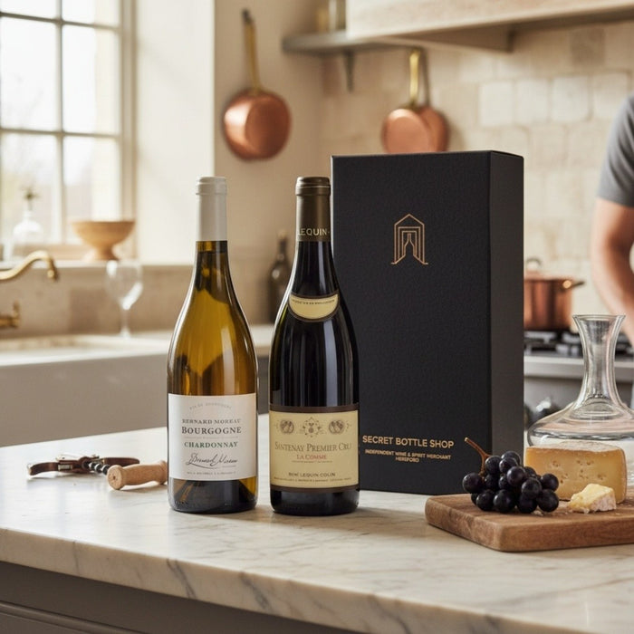 Two wine bottles on a kitchen counter with a gift box and snacks.