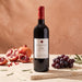 A bottle of Oumsiyat Jaspe red wine stands on a stone slab with pomegranates, grapes, and rosemary props against a warm beige background.