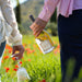 Two people holding a bottle of wine and a glass in a field with flowers and greenery.