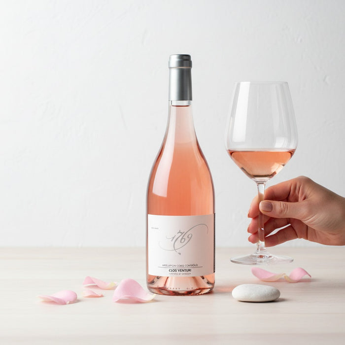 Bottle and glass of rose wine with a hand holding the glass on a light background