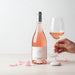 Bottle and glass of rose wine with a hand holding the glass on a light background