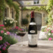 Bottle of Domaine Baron Thenard Givry Rouge 1er Cru Bois Chevaux 2022 and glass on a wooden table with a garden background