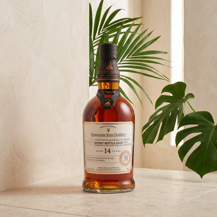 A bottle of Four Squares Rum Distillery 14 Year Old Secret Bottle Shaker rum, placed on a light stone surface with green tropical leaves in the background.
