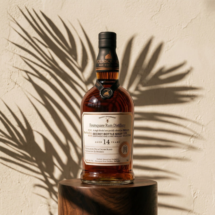 A bottle of Rumsquare Rum Distillery Secret Bottle Shop 14 Year Old Scotch Whisky stands on a dark wooden pedestal against a textured beige wall with dramatic palm leaf shadows.