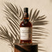 A bottle of Rumsquare Rum Distillery Secret Bottle Shop 14 Year Old Scotch Whisky stands on a dark wooden pedestal against a textured beige wall with dramatic palm leaf shadows.