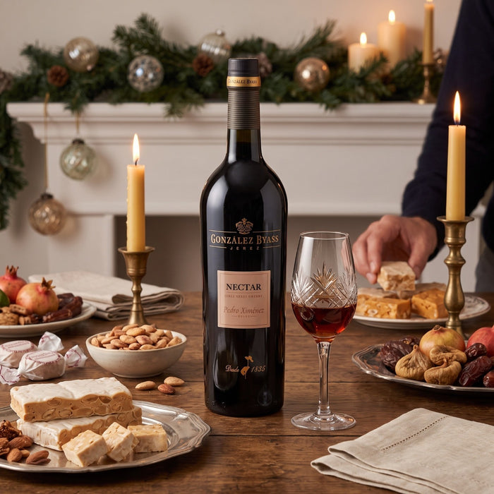 A bottle of Gonzalez Byass Jerez Nectar Sherry stands on a decorated holiday table beside a filled wine glass, with candles, nuts, figs, and pastries in a warm indoor setting.