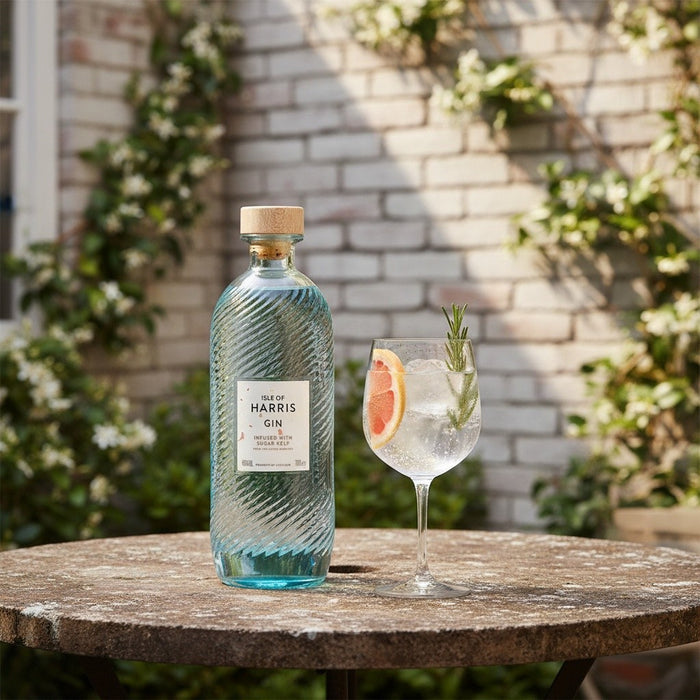 Harris Gin bottle with a glass of gin and tonic on a table outdoors.
