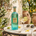 Bottle of Italicus liqueur on a table with a cocktail and lemon slices outdoors.