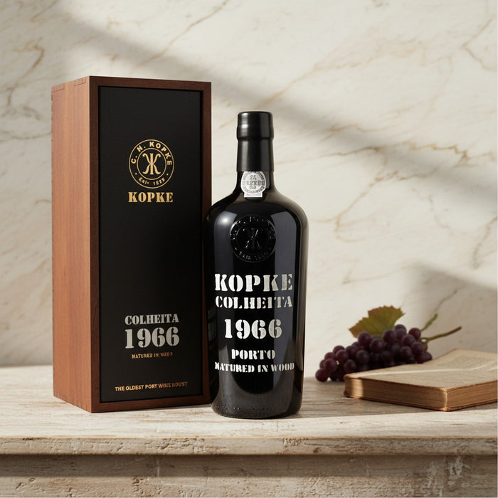 Kopke Colheita 1966 Port wine bottle and box on a wooden surface with grapes and a book.