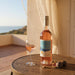 Bottle of rose wine and glass on a wooden table with ocean view