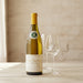 Bottle of Louis Latour Corton Charlemagne Grand Cru and two empty glasses on a wooden surface.