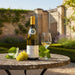 Bottle of Louis Latour Corton Charlemagne Grand Cru with a glass and grapes on a table outdoors.