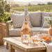 Bottle of Maéa rosé wine with a glass on a wooden table outdoors.