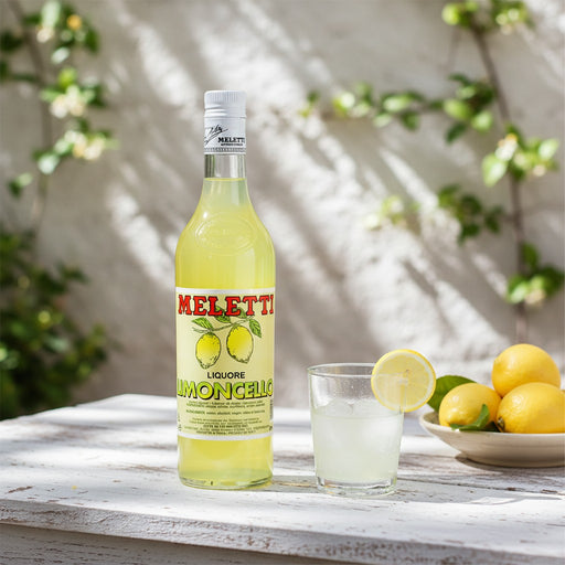 Bottle of Meletti Limoncello with a glass of limoncello and lemons on a wooden table.