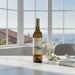 Bottle of Falanghina wine with a glass on a table by a window with a view of the sea.