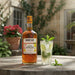 Mount Gay Spiced rum bottle with a cocktail garnished with lime and mint leaves on a wooden table outdoors.