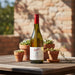 Penfolds wine bottle on a wooden table with potted plants and a stone wall background