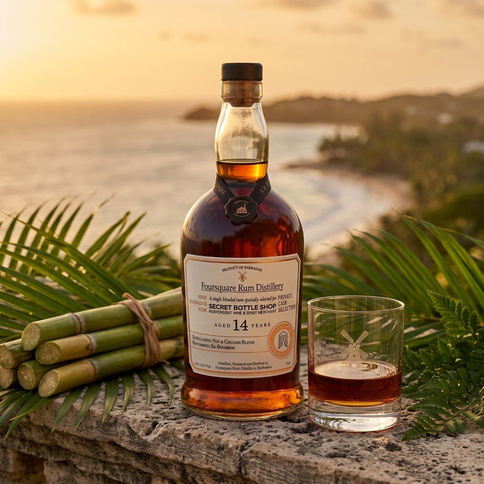 A bottle of Four Square Rum Distillery 14 Year Old rum and a matching glass on a stone ledge, surrounded by green palm leaves and a bundle of sugarcane, with a beach sunset in the background.