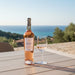 Bottle and glass of rose wine on a wooden table with a scenic background