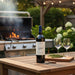 Bottle of wine on a wooden table with a grill and outdoor setting