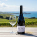 Bottle of Aotea Cabernet Franc wine with a glass on a wooden table in a vineyard setting.