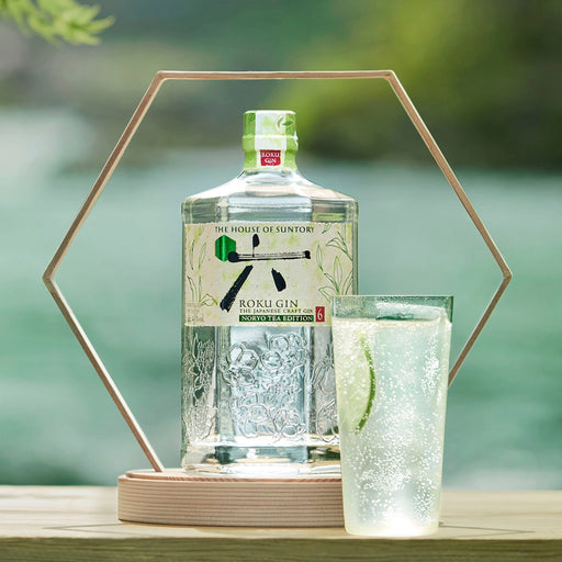 Roku Gin bottle with a glass of gin and tonic on a wooden surface with a blurred natural background