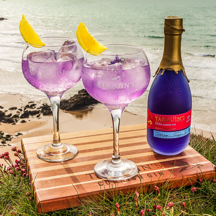Bottle of Tarquins Summer Garden Gin with two Tarquins Glasses and lemon on the beach