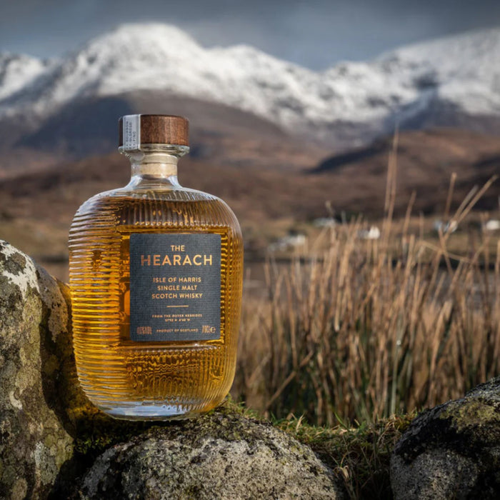 Bottle of The Hearach whisky against a scenic mountain backdrop