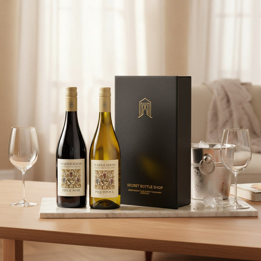 Two wine bottles with a black box on a table with glasses and ice bucket.