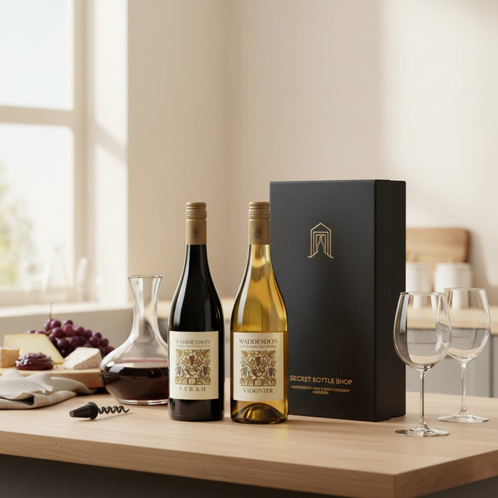 Two wine bottles on a table with a box and glasses in a home setting