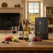 Two wine bottles with glasses and grapes on a wooden table in a cozy room with a fireplace and window view.