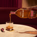 Angels Envy bourbon being poured into a glass on a marble surface with a red curtain background.