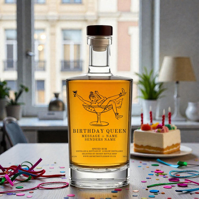 Bottle of 'Birthday Queen' rum with a cake and decorations on a table.