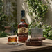 Buffalo Trace whiskey bottle with glass, flask, and smoking cigar on a wooden table outdoors.