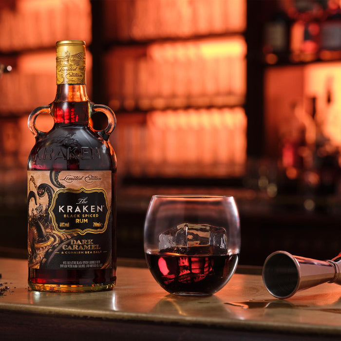Kraken Black Spiced Rum bottle with a glass of rum on a bar counter.