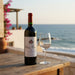 Bottle of Chateau Musar red wine and a glass on a wooden table with a beach background