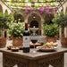 Bottle of wine with a glass on a table outdoors with food and flowers in the background
