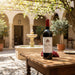 Bottle of wine on a wooden table with a fountain and architectural elements in the background